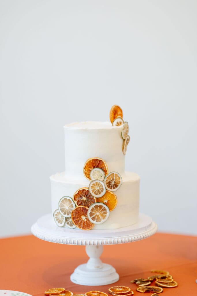 Two-tier white wedding cake decorated with dried citrus slices and displayed on a white cake stand