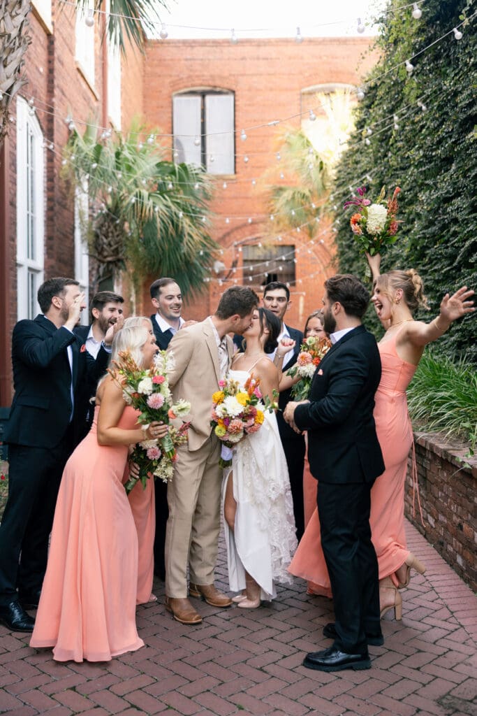 Wedding party gathers around the newlyweds in a brick courtyard, celebrating with colorful florals and joyful expressions at a 701 Whaley Columbia SC wedding.