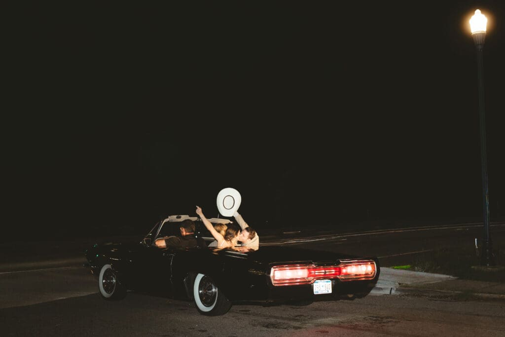 Newlyweds celebrate from a vintage convertible beneath the night sky, an energetic send off following their 701 Whaley wedding reception.