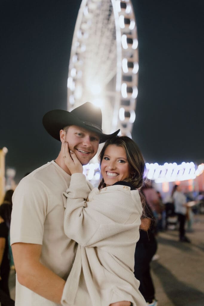 Couple embraces beneath the glow of a Ferris wheel during an evening celebration, showing the playful storytelling possible with Charleston couples photography.
