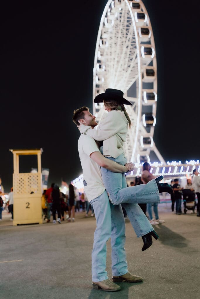 Couple embraces beneath a glowing Ferris wheel at night, creating a playful portrait that shows the personality behind Charleston engagement photos.