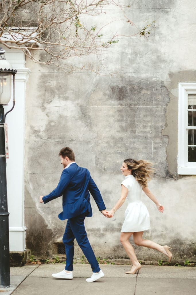 Couple holding hands while walking past a historic building in Charleston, SC