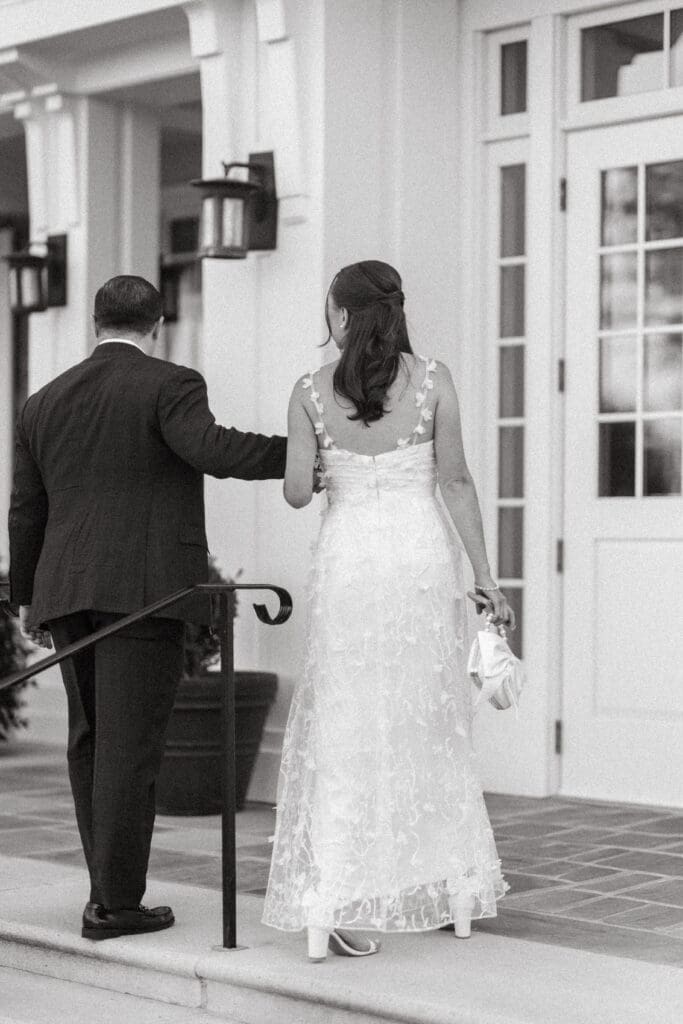 Newlyweds walk hand in hand toward a bright reception entrance in a candid black and white image, part of an authentic Charleston wedding day story.