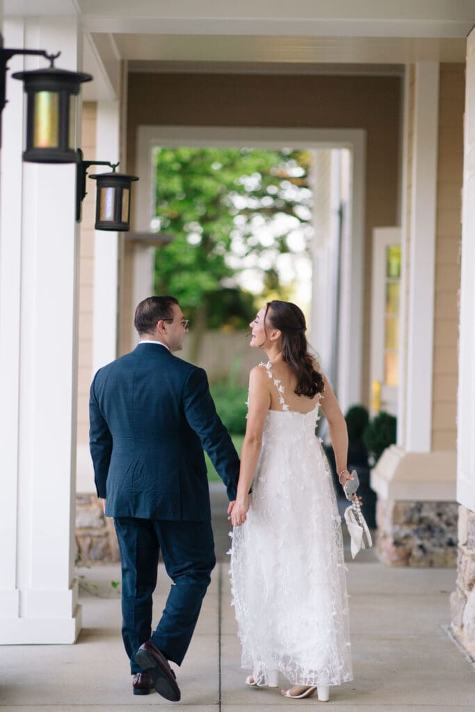 Couple in wedding attire holding hands while walking along a covered walkway