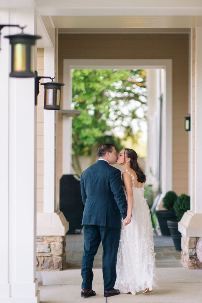Bride and groom share a kiss beneath a covered entrance with soft daylight and greenery beyond, reflecting a romantic Charleston SC wedding photography style.