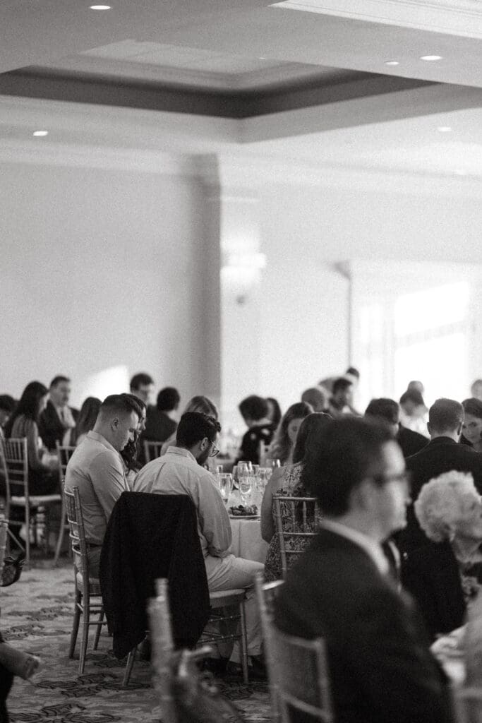 Black-and-white photograph of guests seated at tables during a wedding dinner
