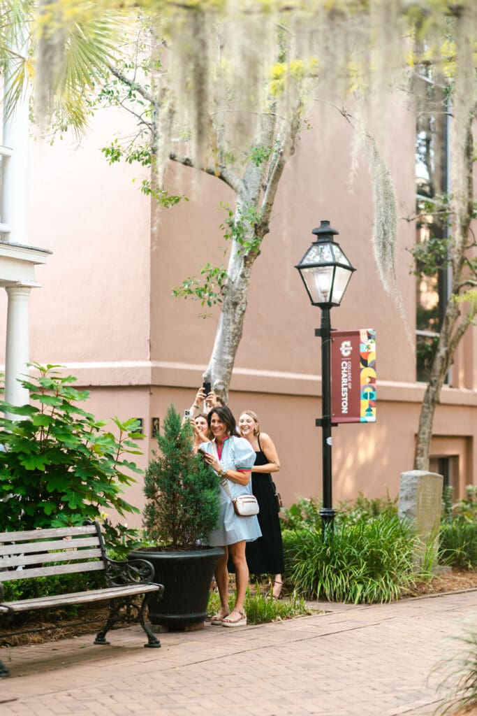 Newly engaged couple embraces near a quiet garden bench, historic pastel building, and traditional streetlamp, highlighting the charm of a downtown Charleston proposal.