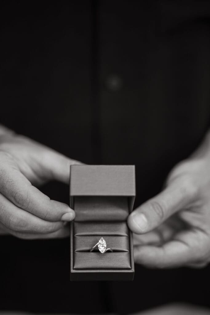 Close-up black-and-white photograph of a diamond engagement ring in an open ring box