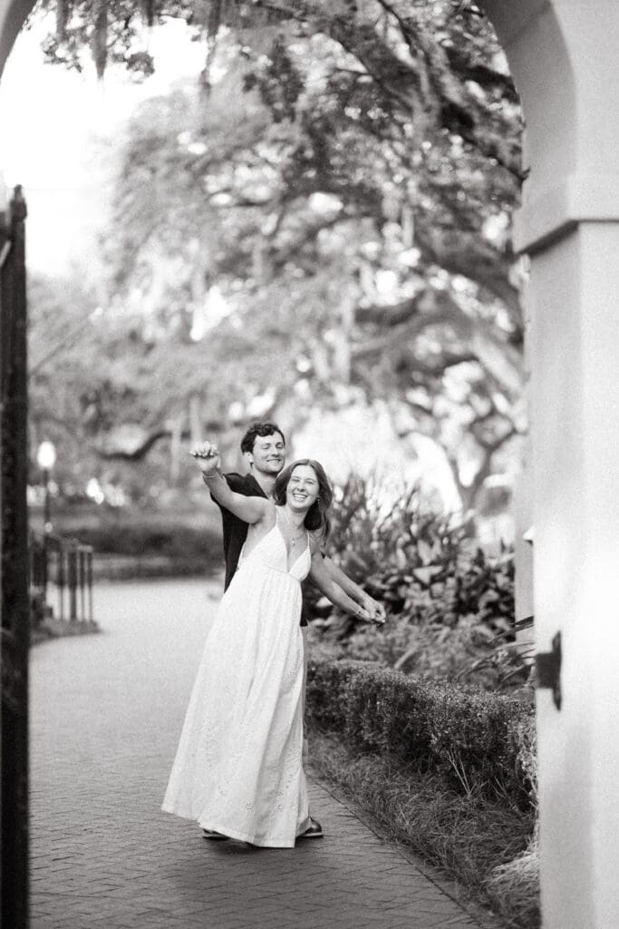Woman smiles as her partner embraces her from behind beneath an arched walkway, an intimate moment inspired by documentary style Charleston couples photography.
