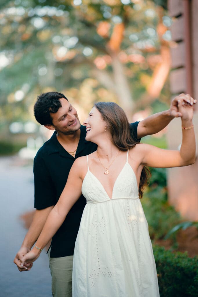 Couple walks hand in hand while playfully dancing along a tree lined path, reflecting the candid approach of a wedding photographer in Charleston SC.