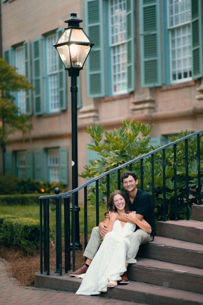 Couple sitting together on the steps of a historic Charleston home during an engagement session