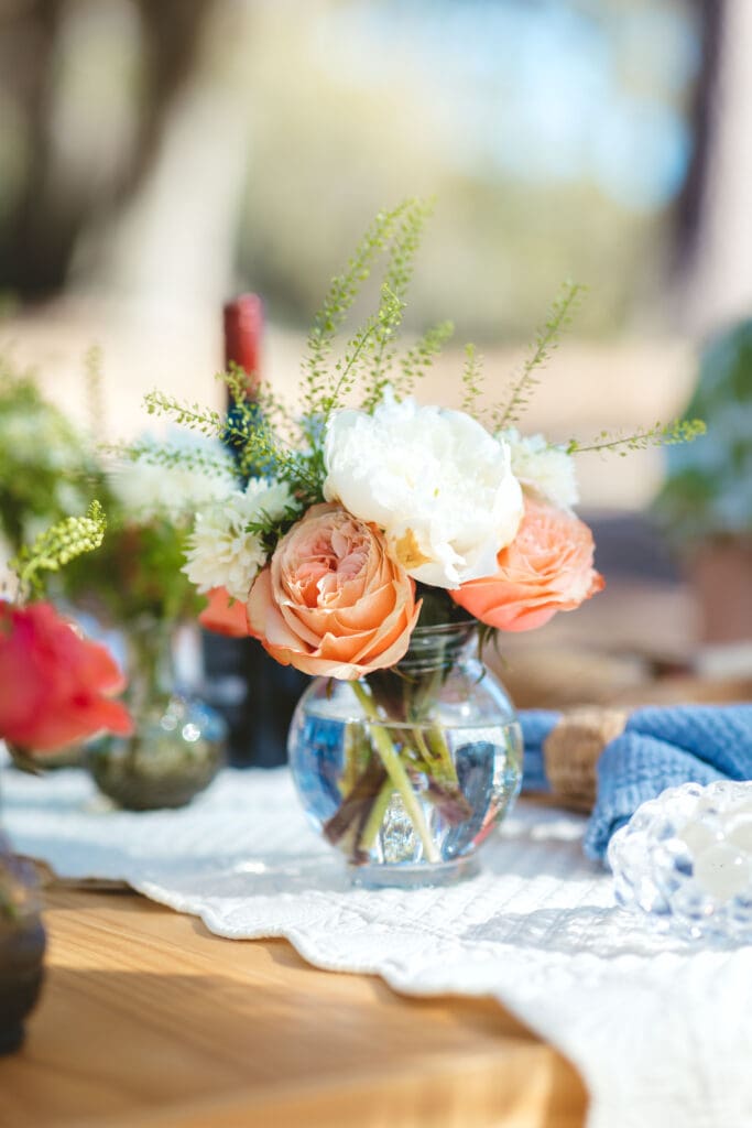 Peach and white floral centerpiece in a glass vase on a decorated dinner table