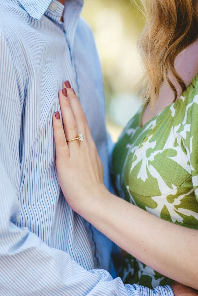Close up of a woman displaying her engagement ring while resting her hand on her partner’s chest, a personal detail to consider when envisioning intimate wedding venues in Charleston SC.
