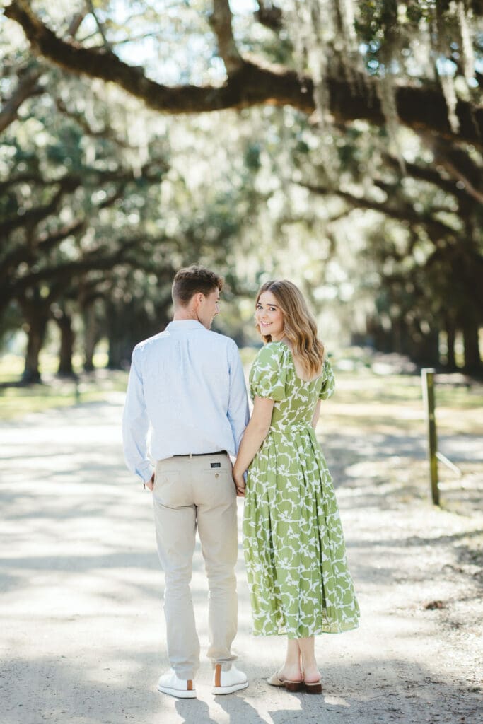 Couple walks beneath sweeping live oak branches and Spanish moss, illustrating the natural setting couples may prioritize when comparing outdoor wedding venues in Charleston SC.