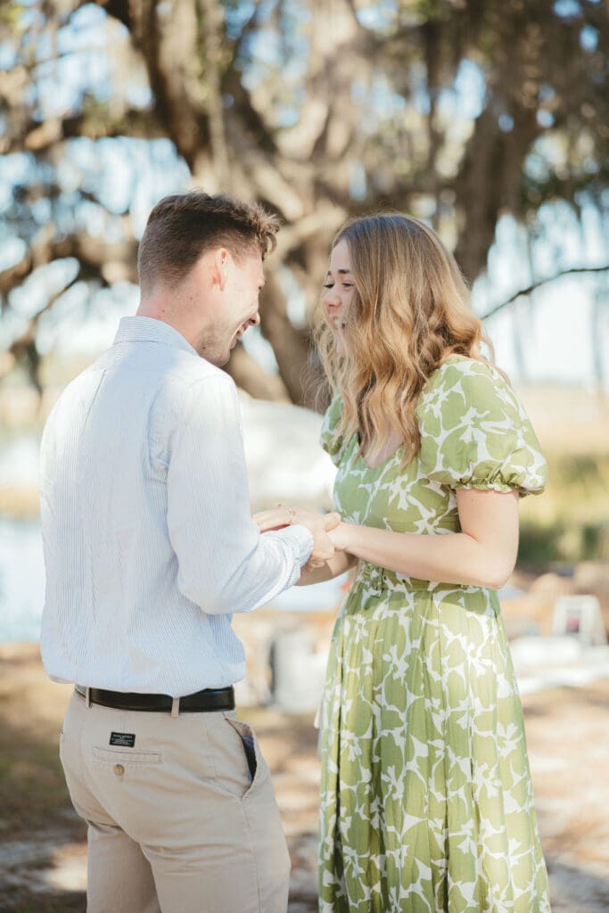 Couple holds hands and smiles beneath a canopy of Spanish moss after getting engaged, surrounded by the natural beauty of a romantic Charleston SC proposal spot.