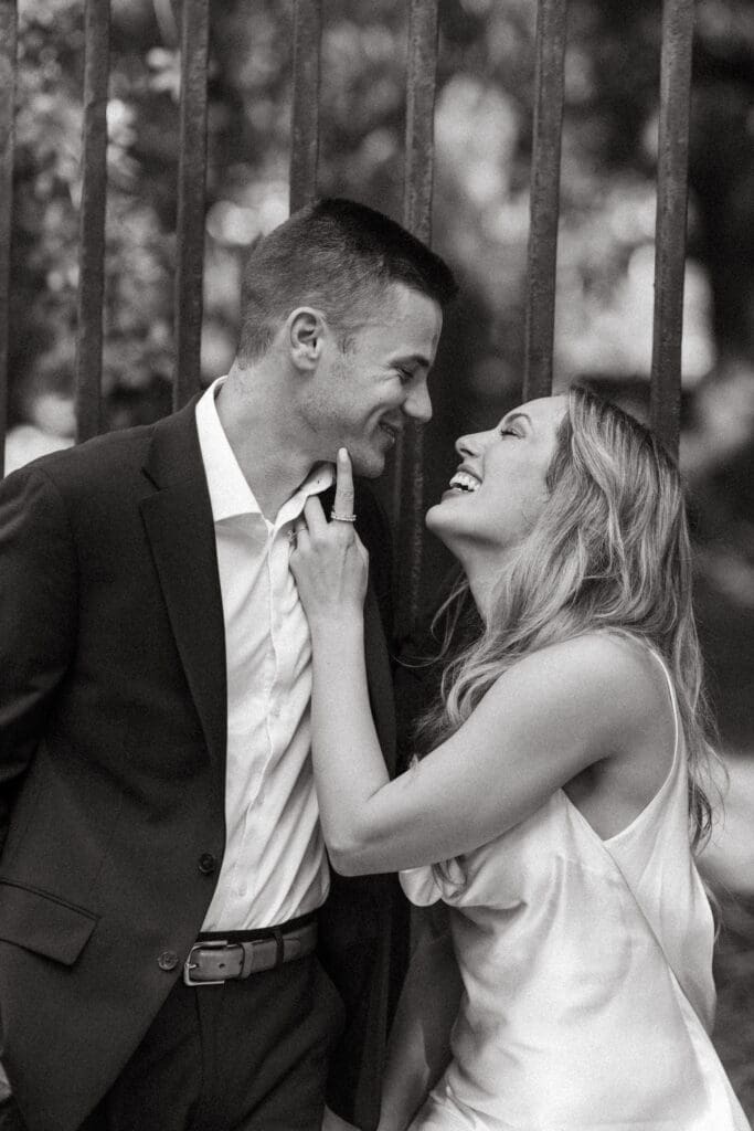 Couple laughs together during a close black and white portrait among tall trees, capturing the easy connection of natural Charleston wedding photography.