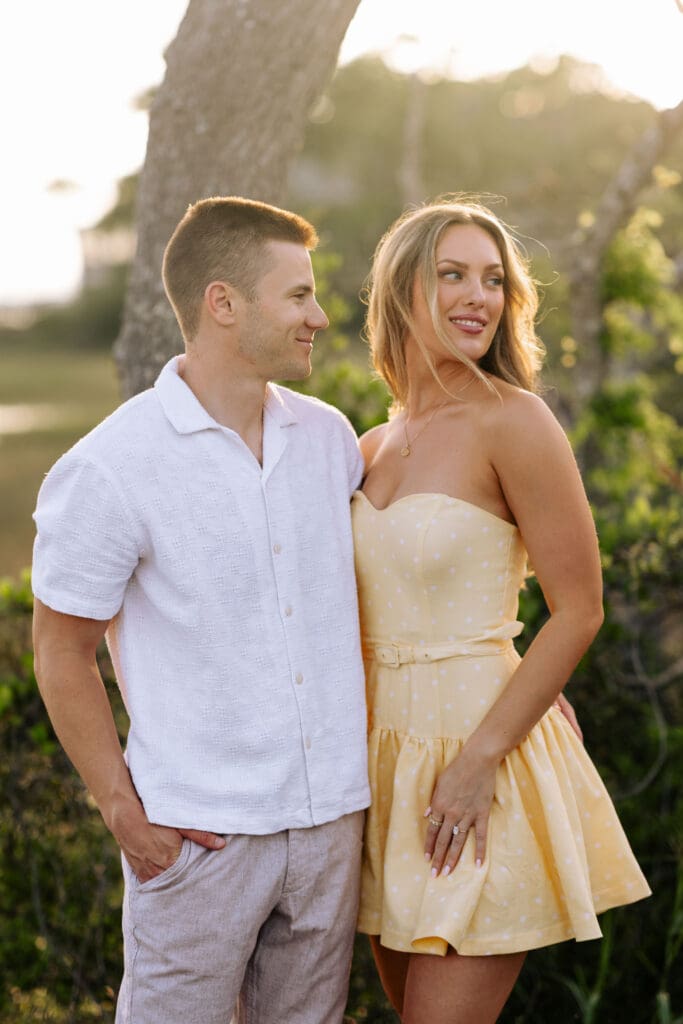 Couple stands together in warm golden light, dressed in relaxed summer attire for an elegant Charleston SC engagement photography session.