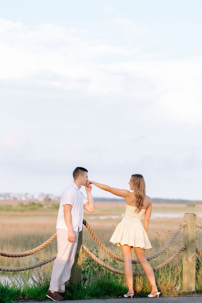 Playful couple holds hands beside an expansive Lowcountry marsh, adding movement and personality to their Charleston SC engagement photos.