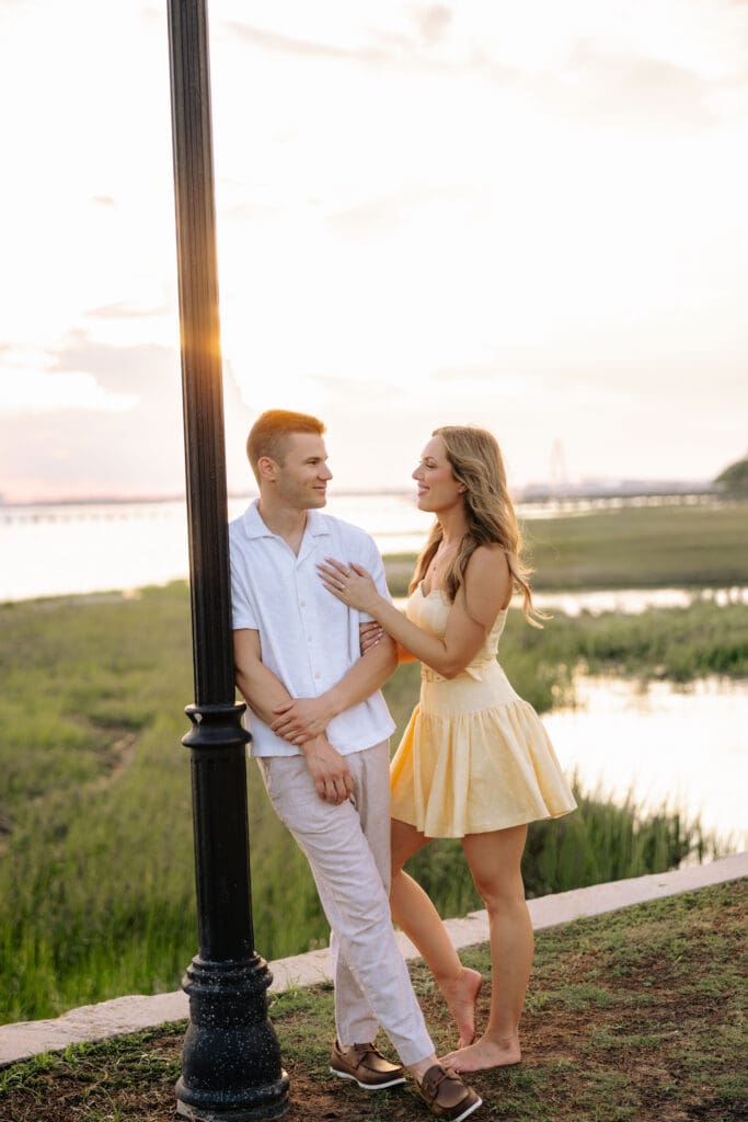 Couple stands beside the marsh at golden hour as sunlight filters around them, blending romantic portraits with the coastal scenery near downtown Charleston.
