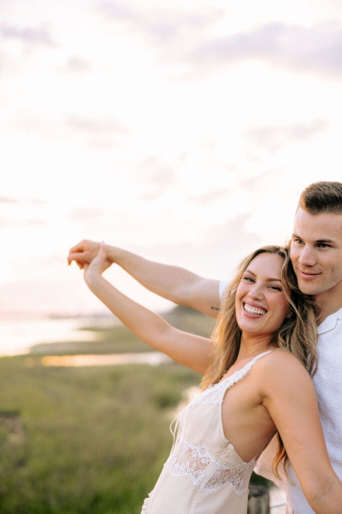 Smiling couple embraces against expansive marsh views at sunset, illustrating the open scenery couples love in a waterfront wedding venue Charleston SC.