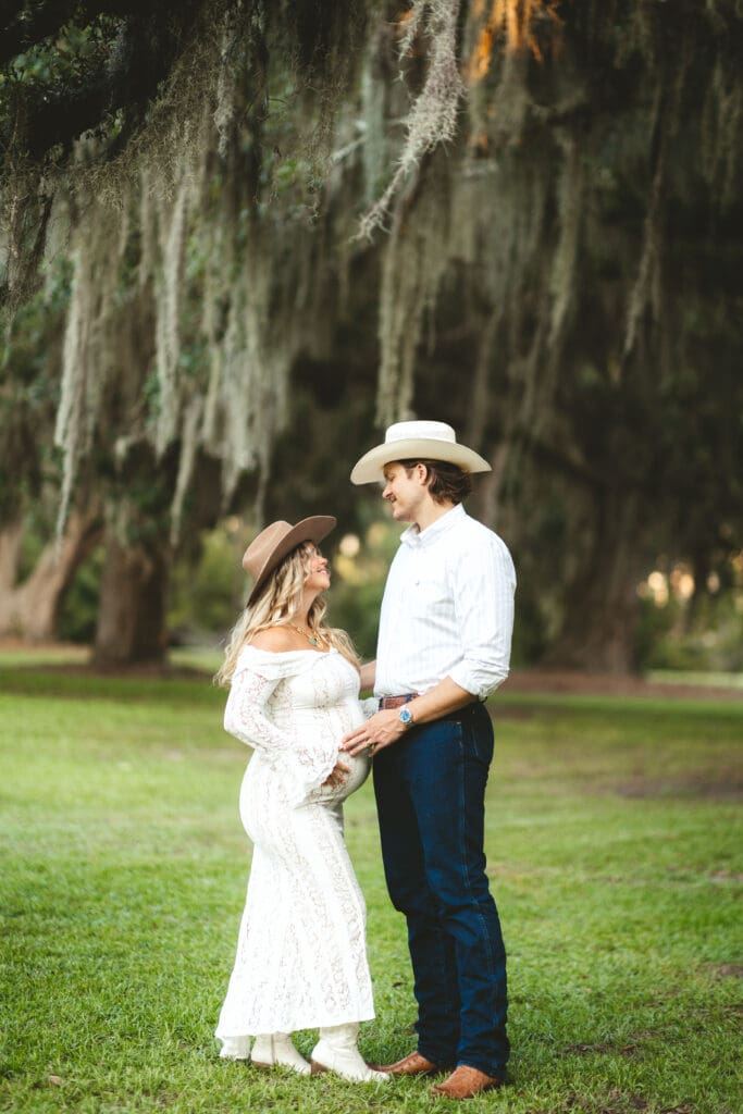 Couple pauses together on a green lawn beneath sweeping Spanish moss, capturing the natural Southern character associated with Creek Club I’On photography.