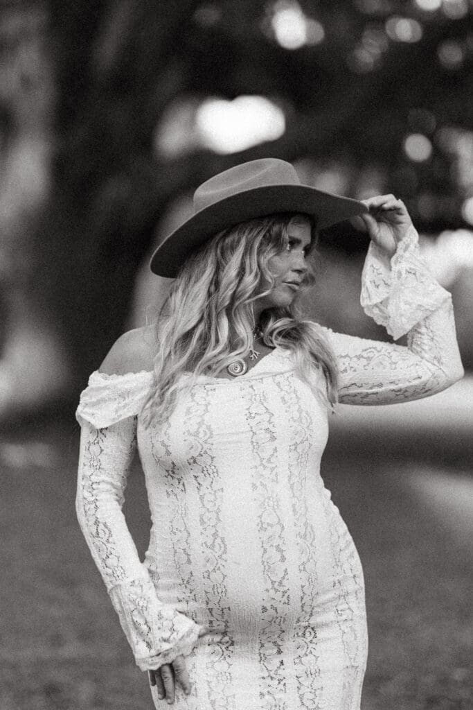 Black and white maternity portrait of an expectant mother in a lace dress and wide brim hat, photographed with an editorial approach near Creek Club at I’On.